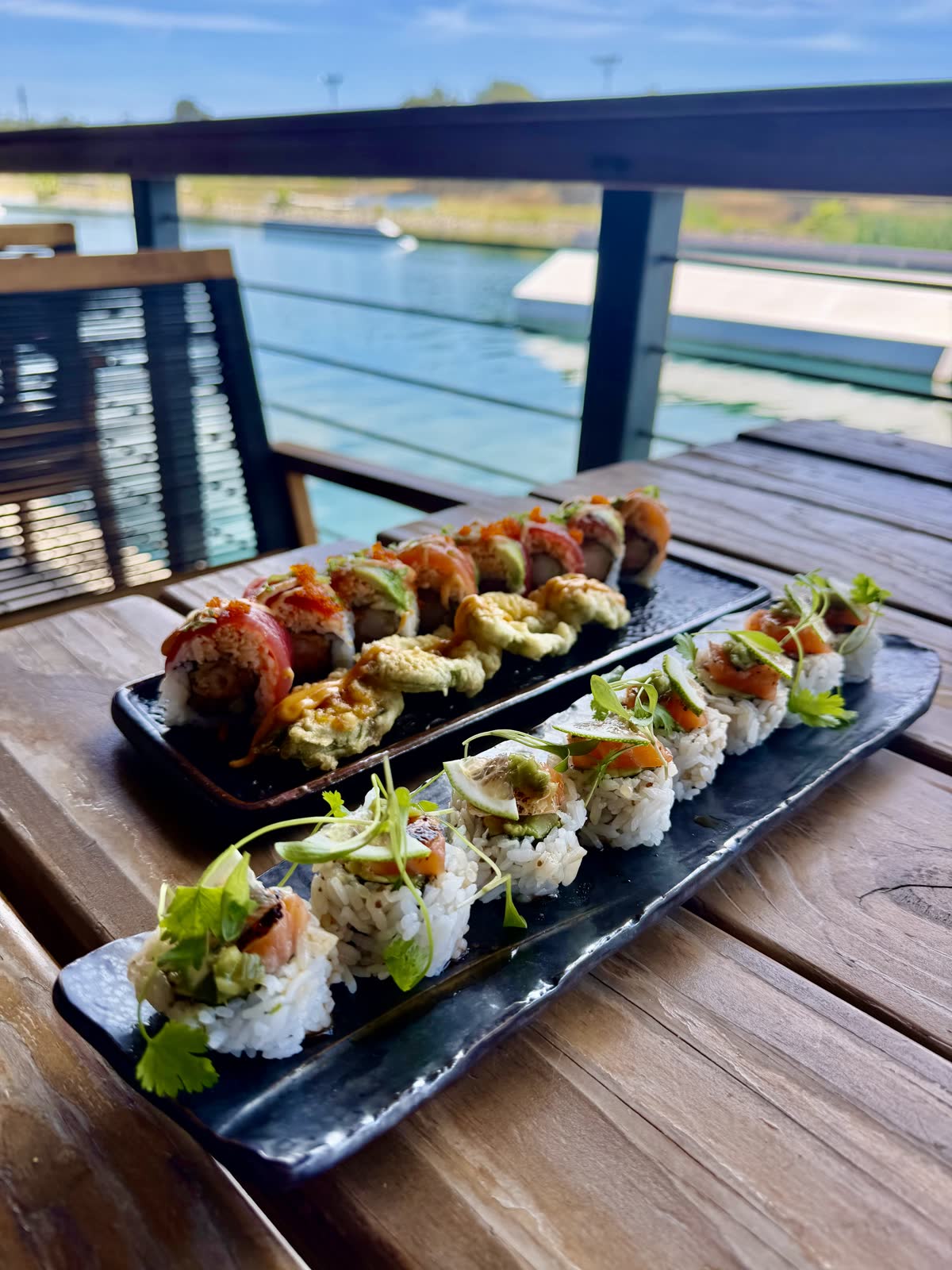 Two sushi platters on a deck table with the turquoise lake behind